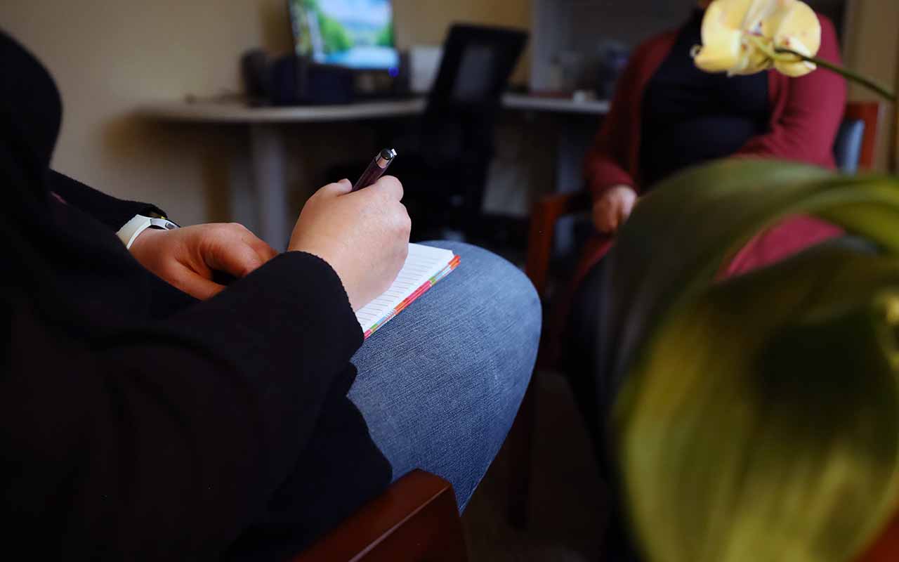 A color photograph of a counselor taking notes during a meeting with a guest at the Solanus Casey Center.