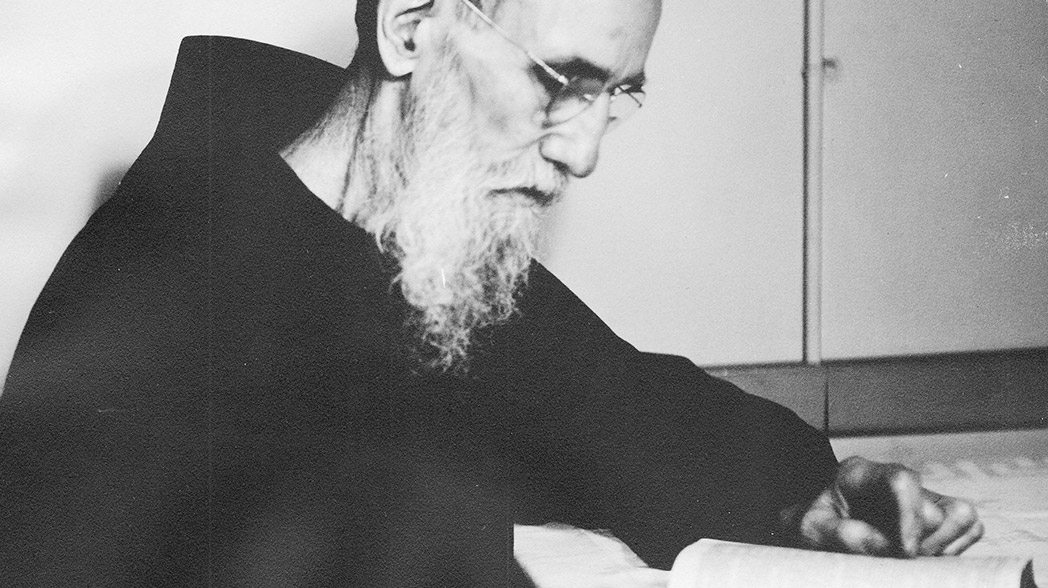 Black-and-white photograph of Blessed Solanus Casey seated at a desk writing in a notebook.
