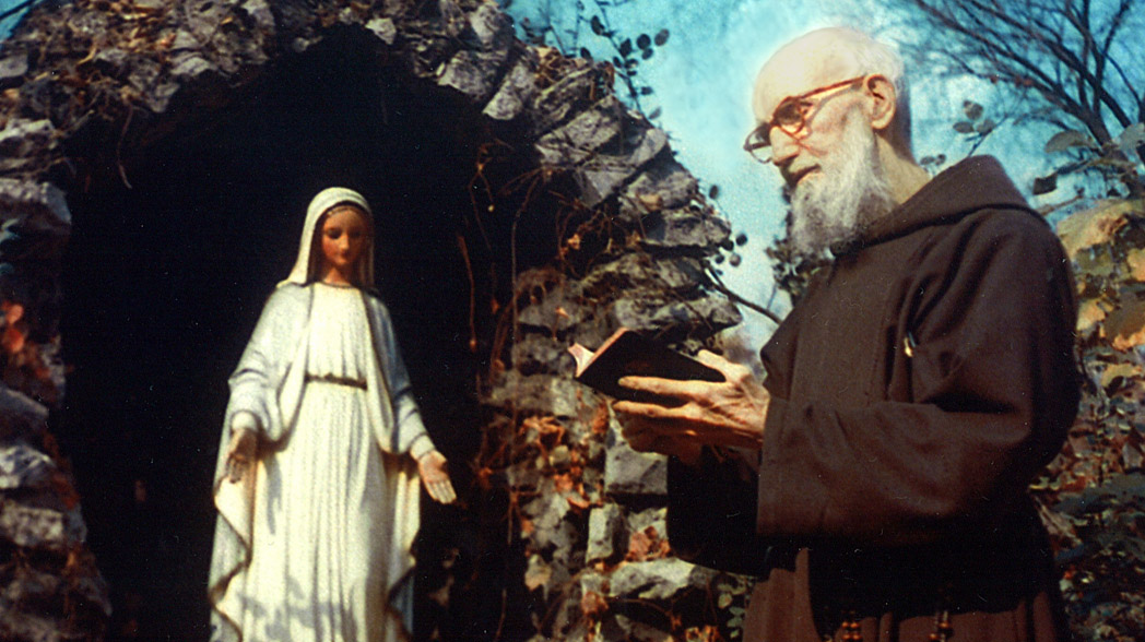Blessed Solanus Casey pictured in a color photograph at the Grotto in the backyard of St. Bonaventure Monastery in Detroit. Solanus holds and is reading a breviary or other book. Photo circa 1956-1957.