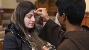 Close-up photo of a Capuchin friar distributing ashes on the forehead of a female Massgoer on Ash Wednesday 2022 at St. Bonaventure Chapel.
