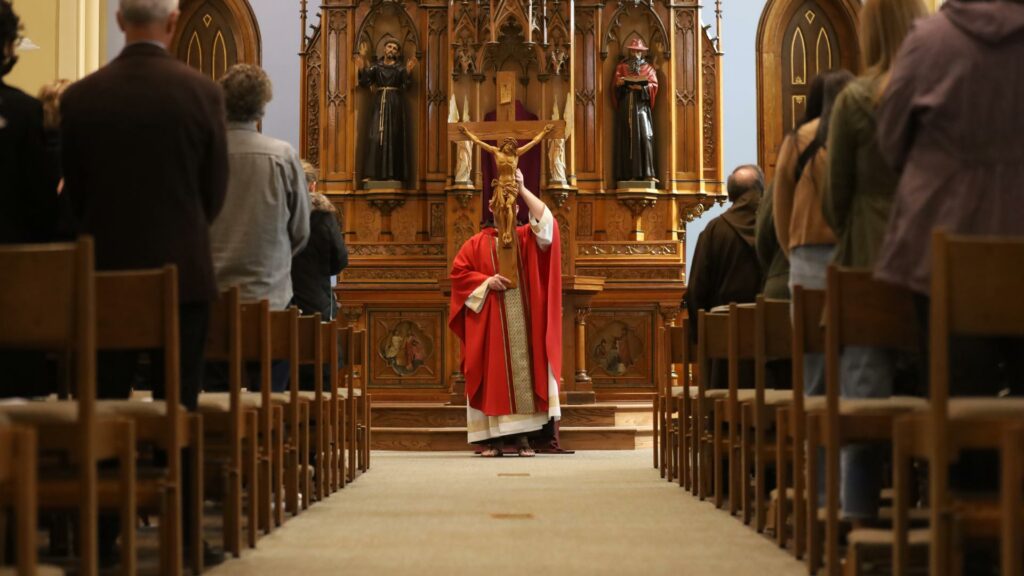Color photo of veneration of the Cross from Good Friday Liturdy 2023. Br. Igor De Bliquy, OFM Cap. hold the cross aloft in the sanctuary of St. Bonaventure Chapel.