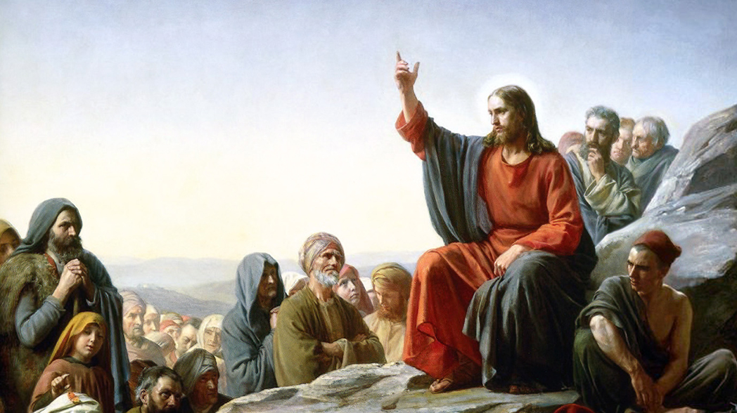 Jesus sitting on top of a mountain surrounded by those listening to him.