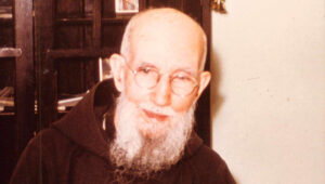 Blessed Solanus Casey smiles behind his desk.